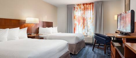 A hotel room with two beds, a desk with a television, a lamp, and a window with curtains.