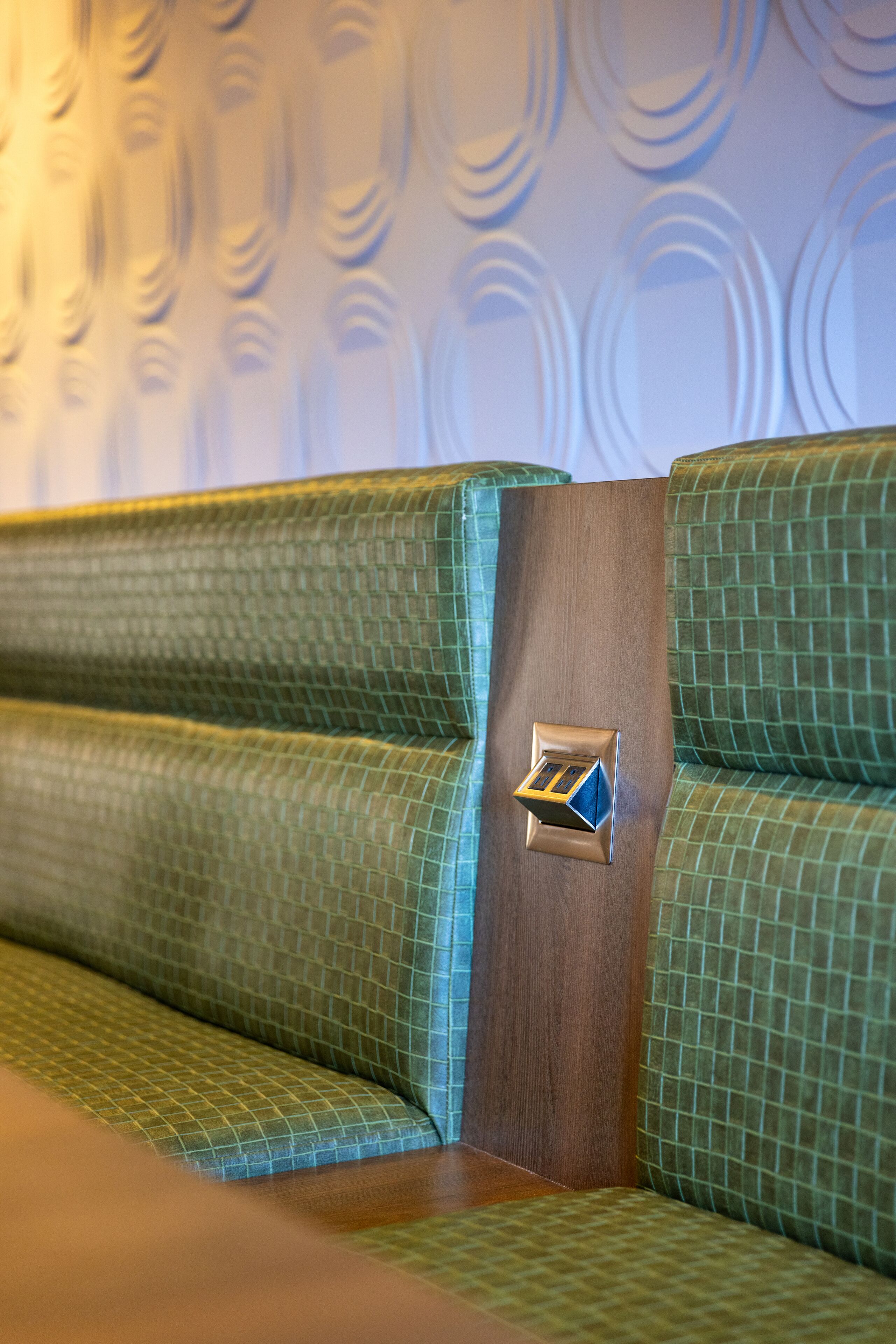 Une partie d’un banc recouvert d’un tissu vert, agrémenté d’un élément décoratif en bois, qui fait probablement partie d’un espace détente dans un hôtel ou un établissement similaire.