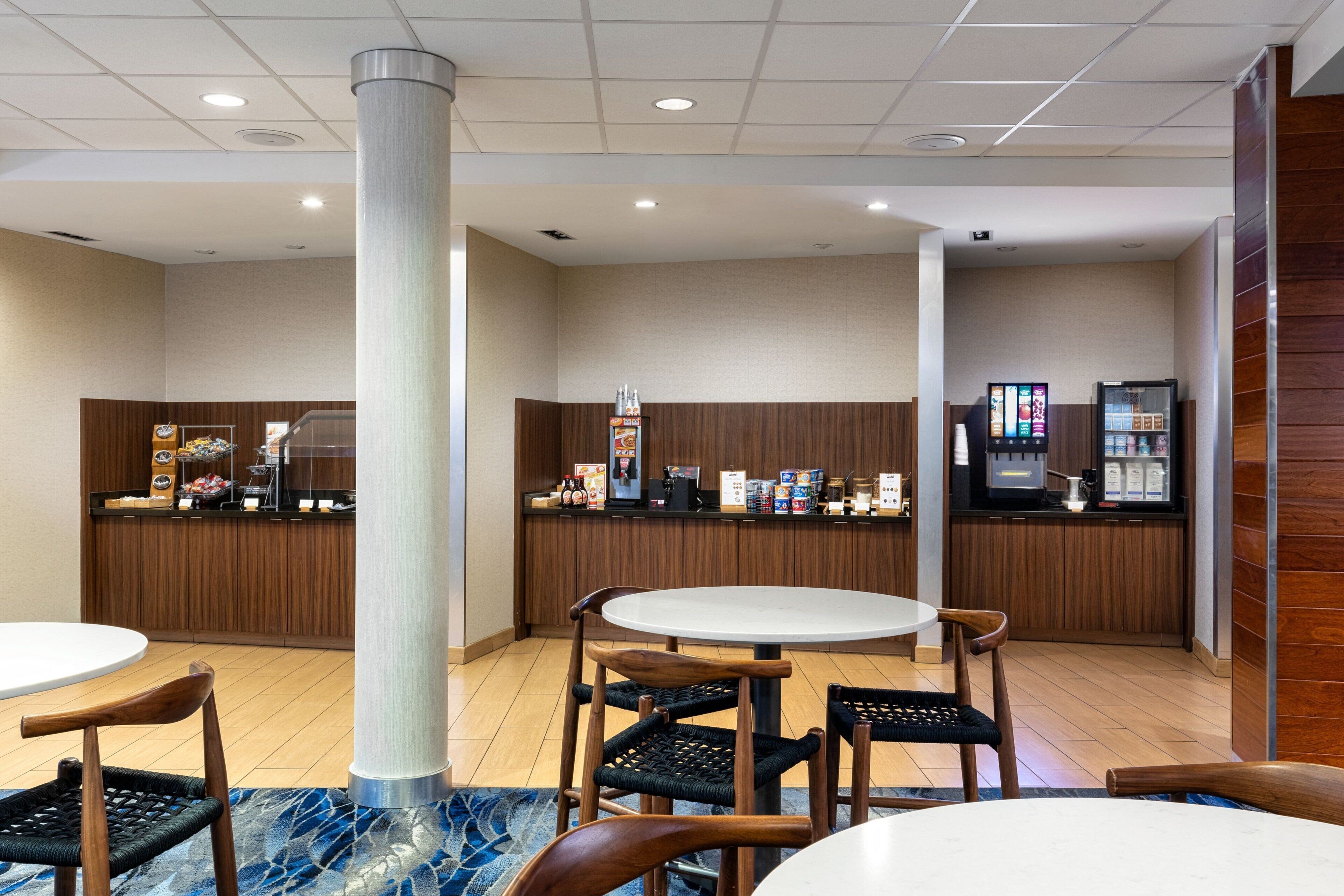 A hotel lobby with a reception desk, a coffee machine, and seating area with round tables and chairs.