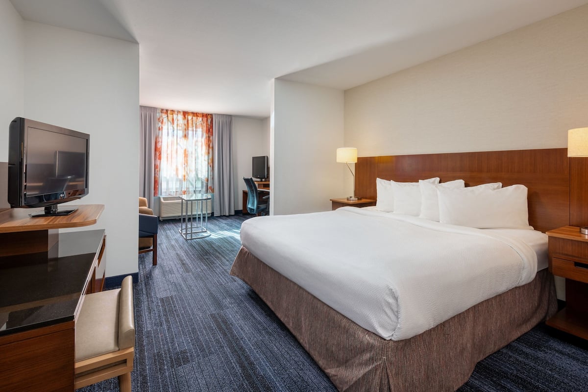 Une chambre d’hôtel avec un grand lit, un bureau avec une télévision, une chaise et une lampe.