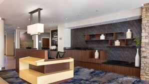 Een modern receptiebalie met een houten afwerking en een lichtgekleurd aanrechtblad. Daarboven bevinden zich houten planken, en aan de rechterkant een stenen muur met een donkere, structuurrijke afwerking.