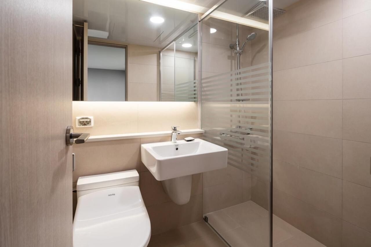 Un baño moderno con inodoro, lavamanos y cabina de ducha con mampara de vidrio.