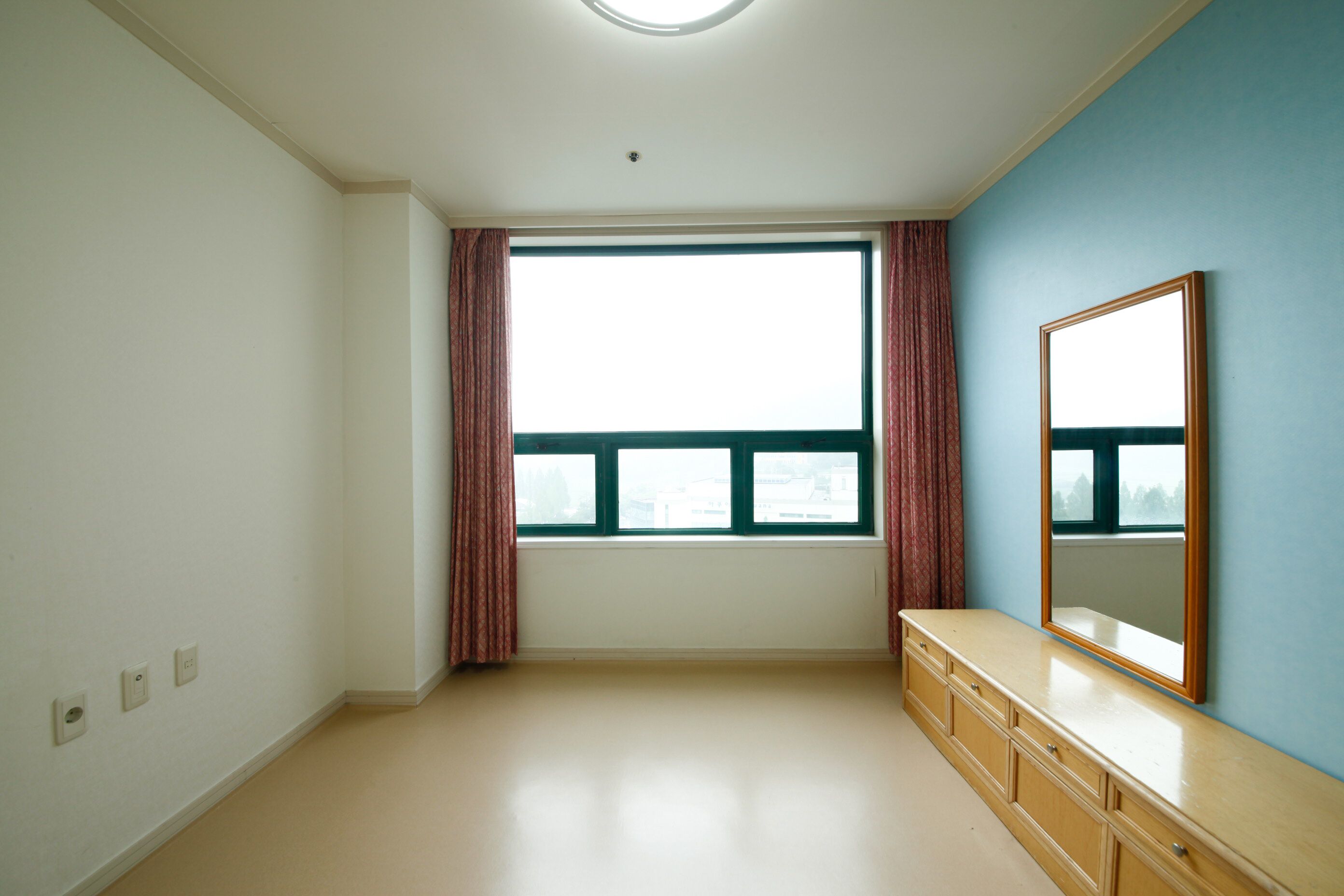 A room with a large window, a dresser, and a mirror on the wall.