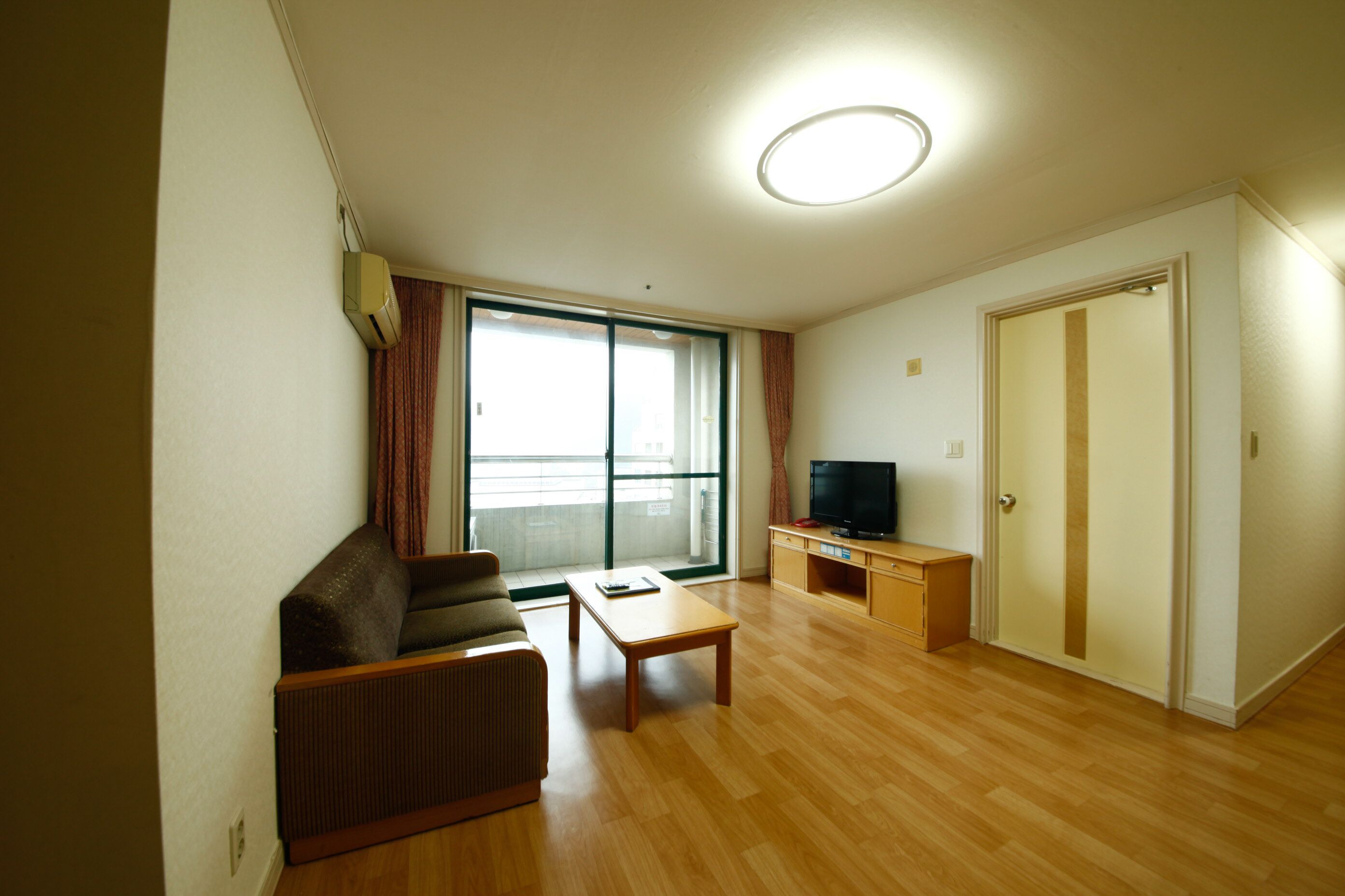 A living room with a sofa, a coffee table, a television on a stand, and a sliding glass door leading to a balcony.