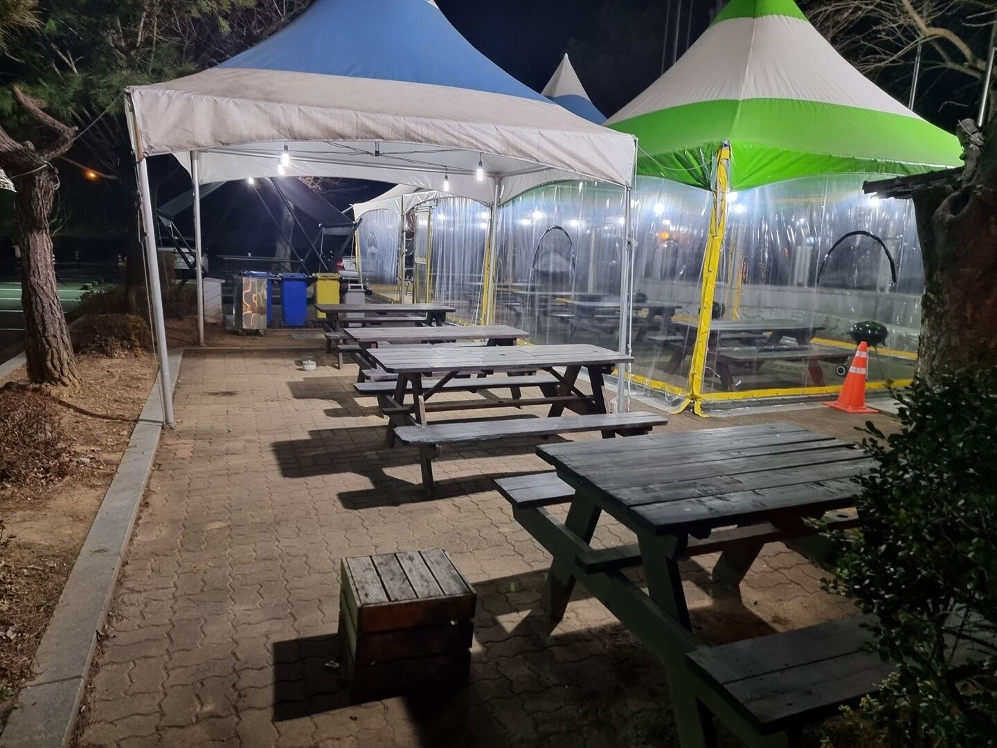A series of outdoor picnic tables under clear canopies, with a trash bin and a small wooden box nearby.