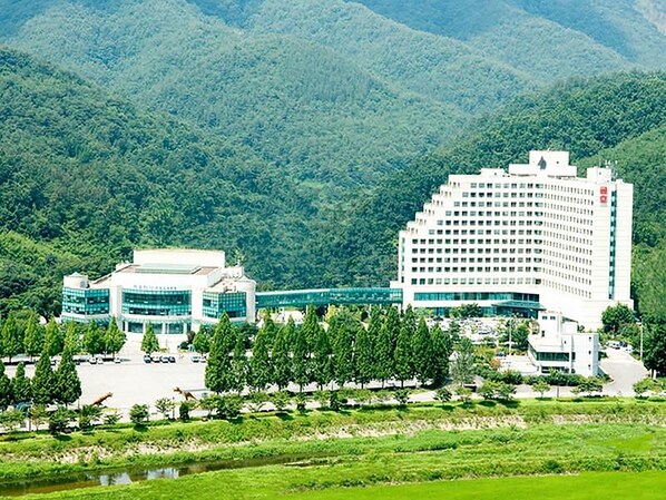 Un hotel moderno con un edificio grande y una extensión más pequeña, rodeado de vegetación exuberante y montañas al fondo.