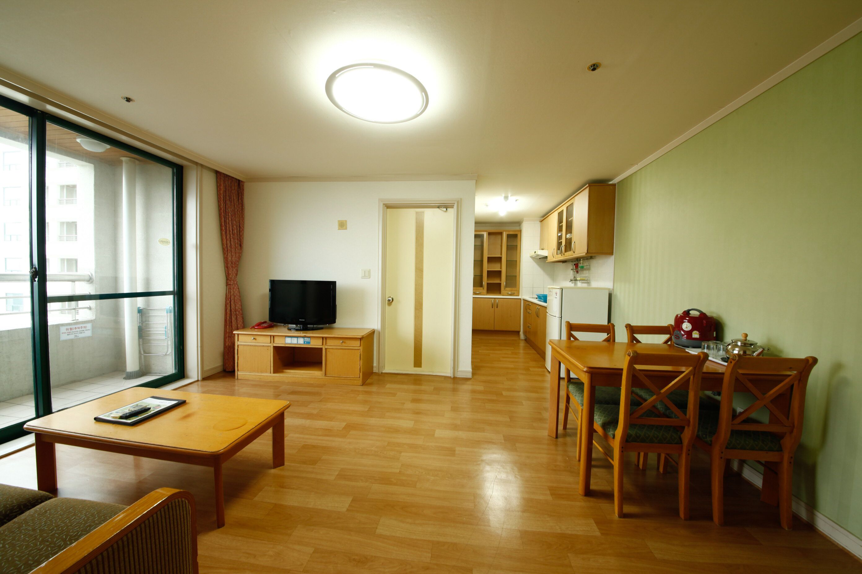 A living room with a sofa, a wooden coffee table, a TV on a stand, and a dining area with a table and chairs.