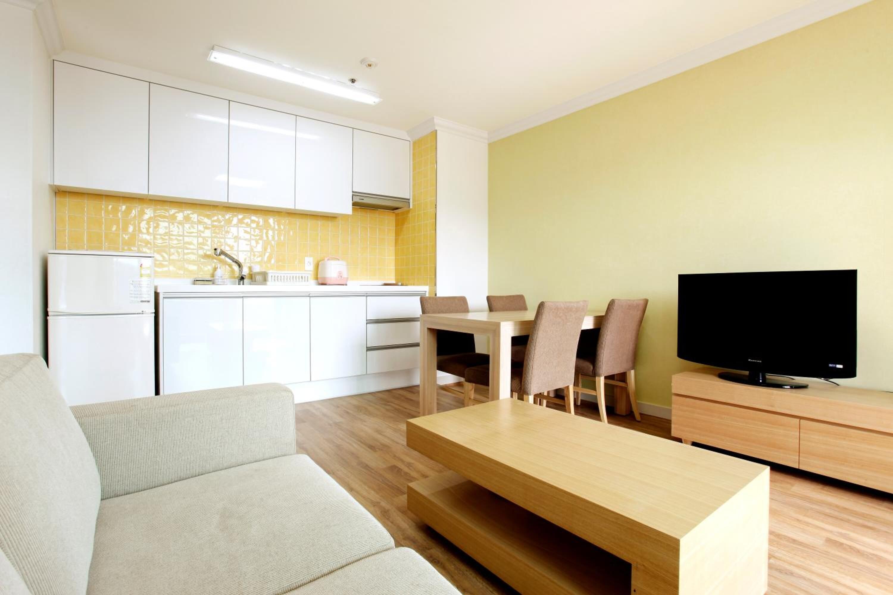 A modern living room with a sofa, a wooden coffee table, a TV on a wooden stand, and a dining area with chairs and a table.