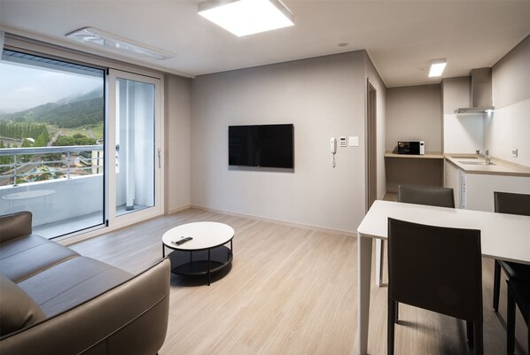 Una habitación de hotel moderna con balcón, televisor de pantalla plana, zona de comedor y kitchenette.