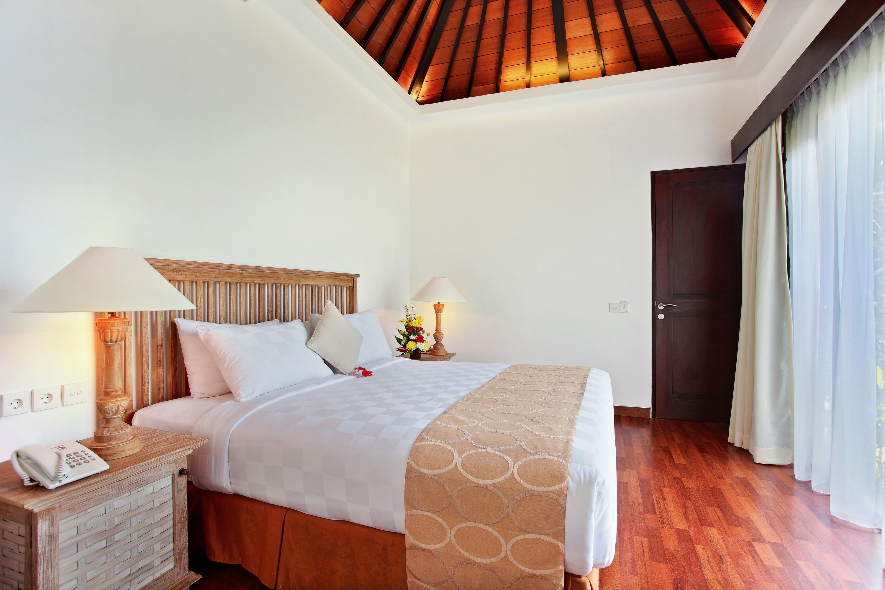 A hotel room with a wooden headboard, a bed with white linens, a wooden nightstand with a lamp, and a wooden ceiling.