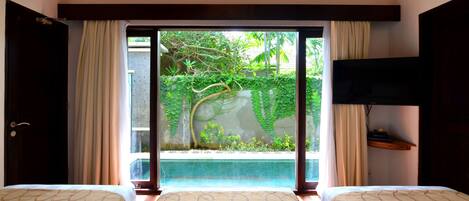 A hotel room with two beds, a large window with a view of a garden and a pool, and a flat-screen TV mounted on the wall.