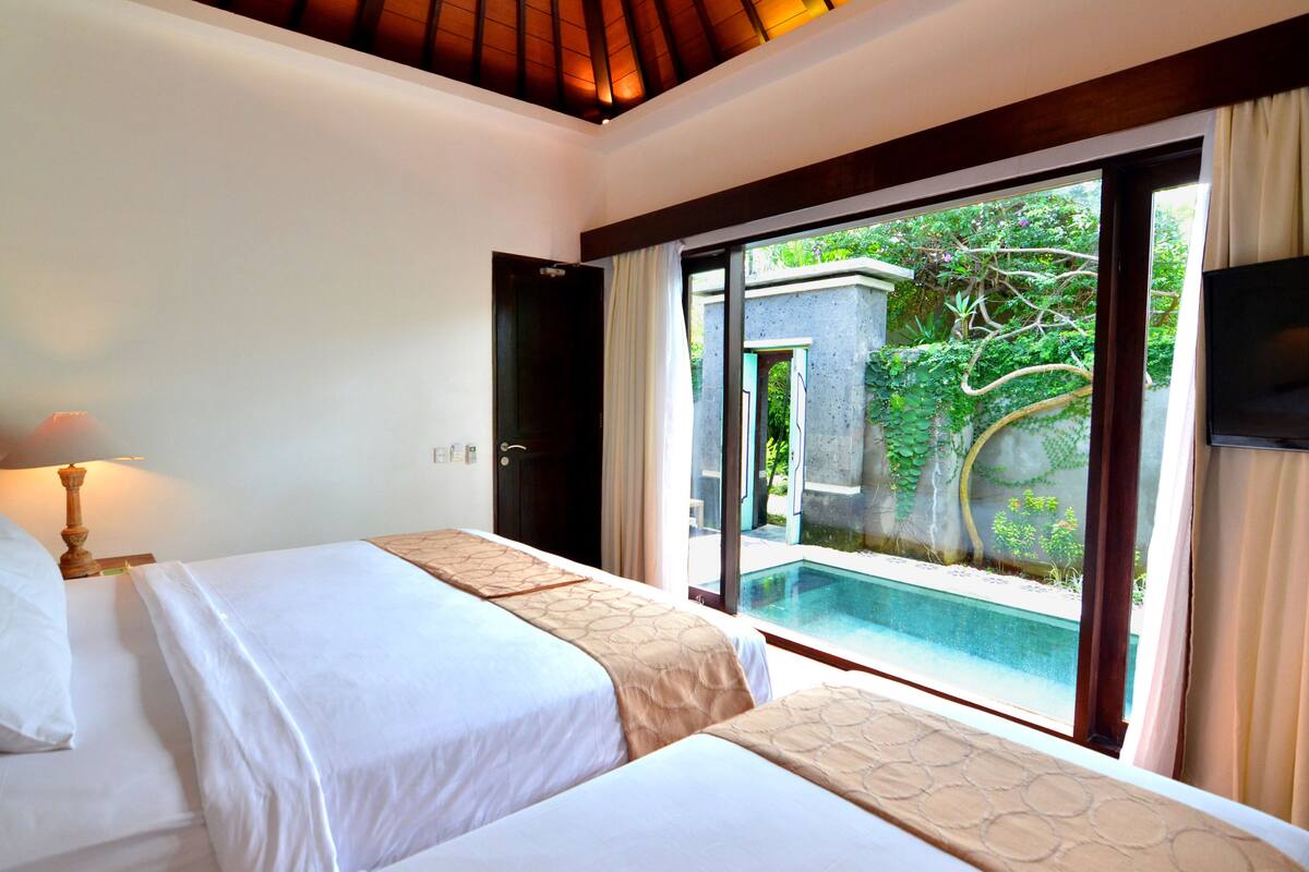 A hotel room with two beds, a TV, and a view of a swimming pool.