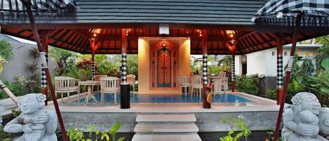 A covered outdoor area with a pool, seating, and decorative statues.