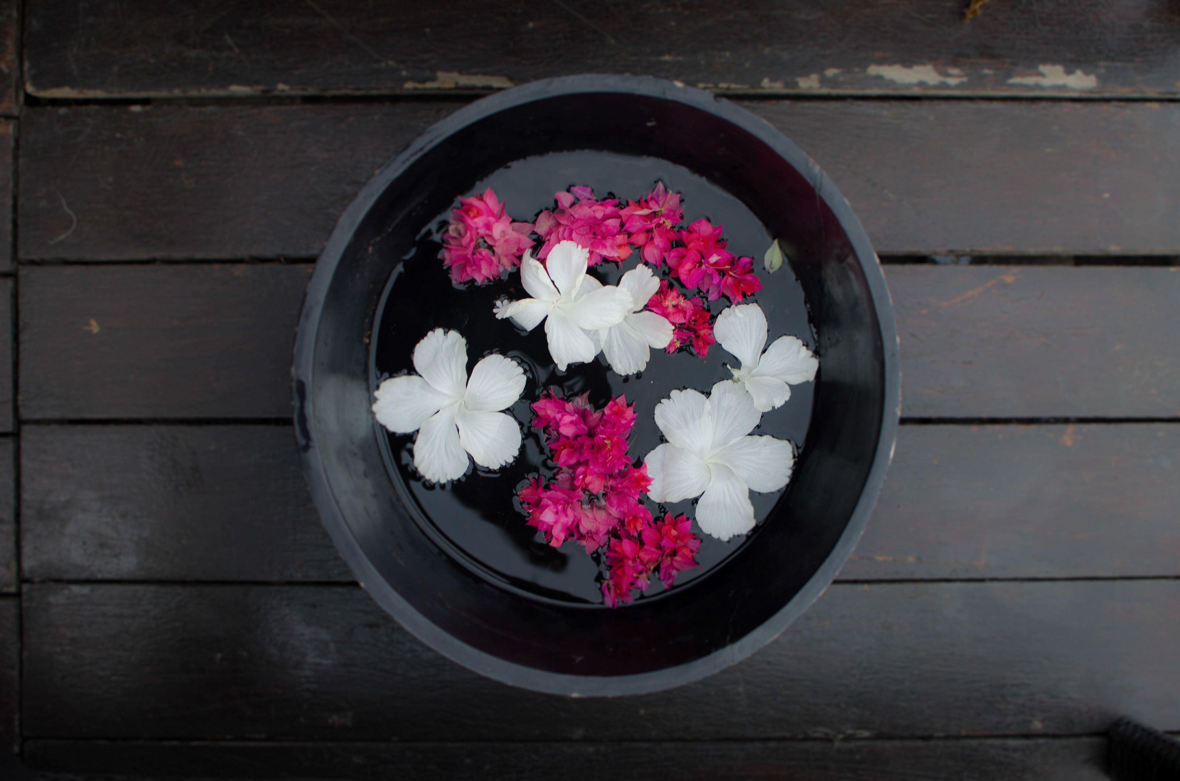 A black bowl containing white and pink flowers on a wooden surface.