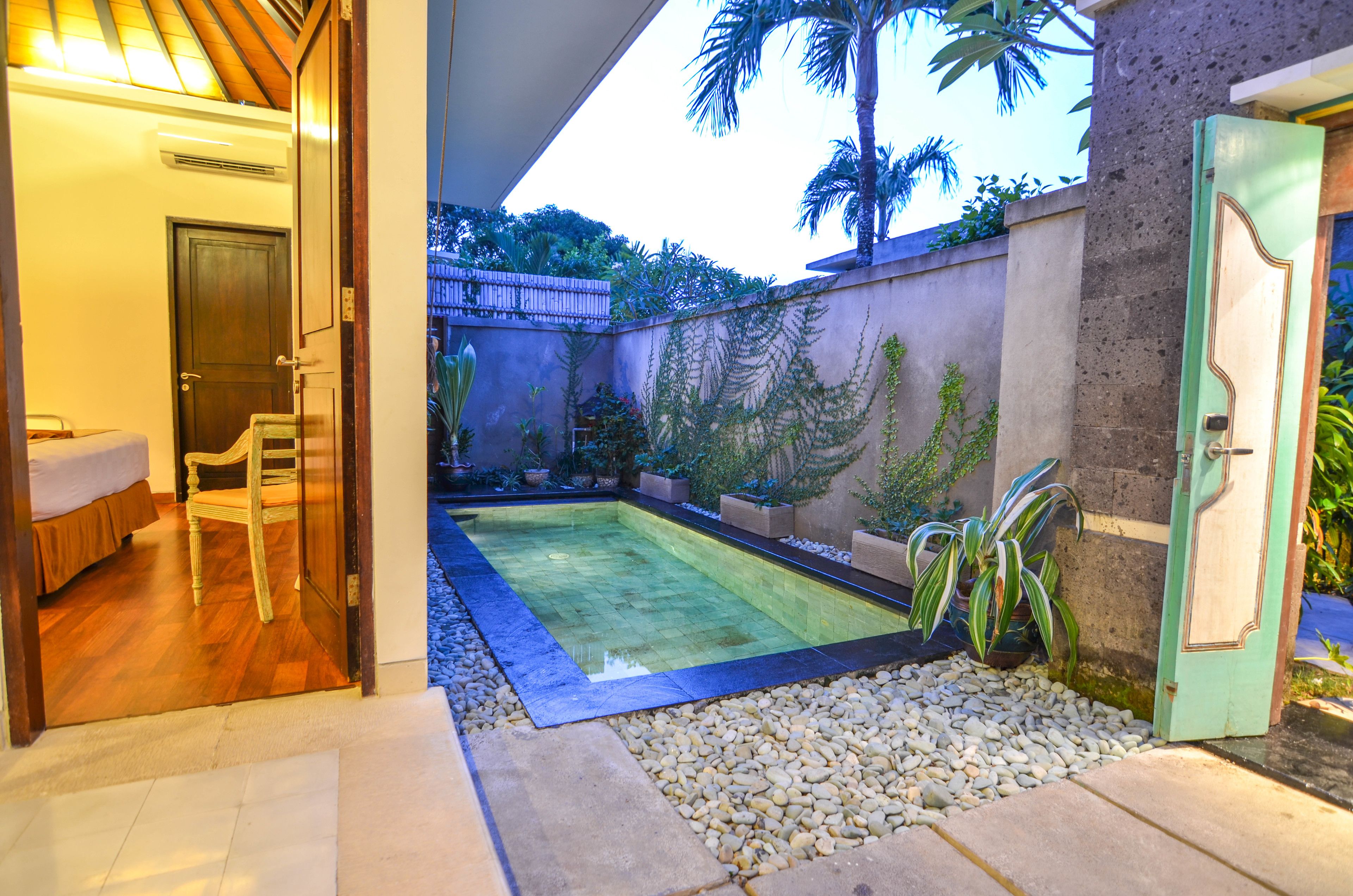 A swimming pool with a tiled deck, surrounded by a stone wall and potted plants.