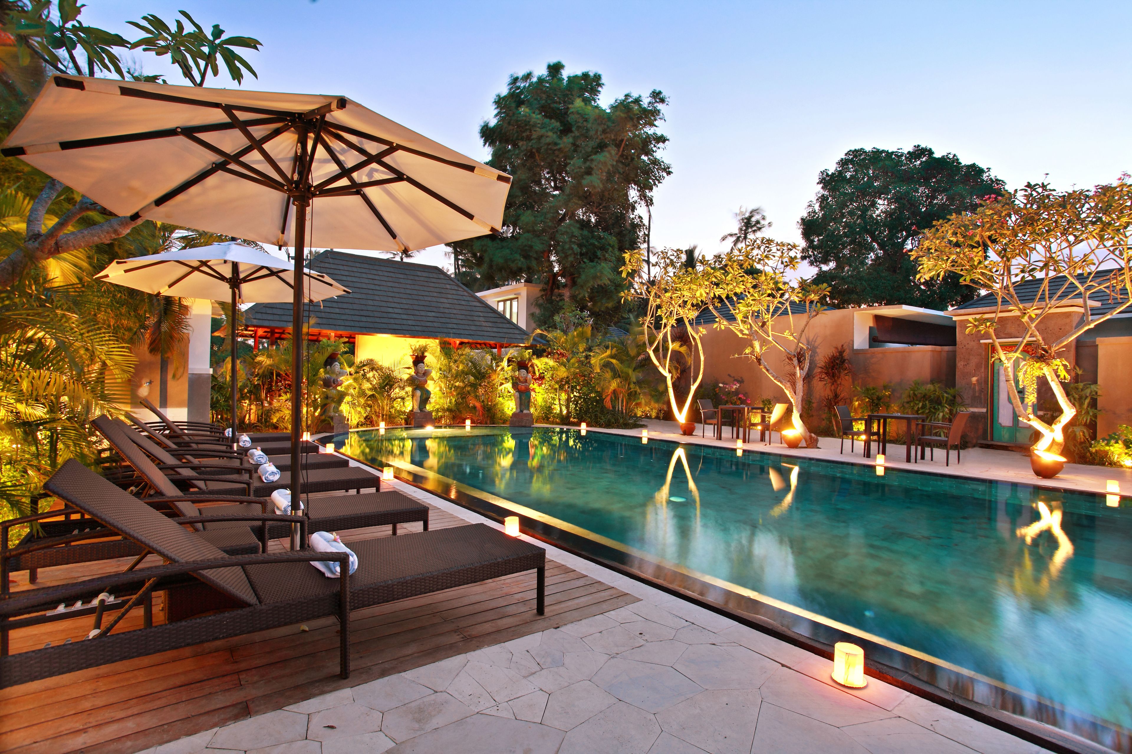 A poolside area with lounge chairs and umbrellas, surrounded by lush greenery and trees.