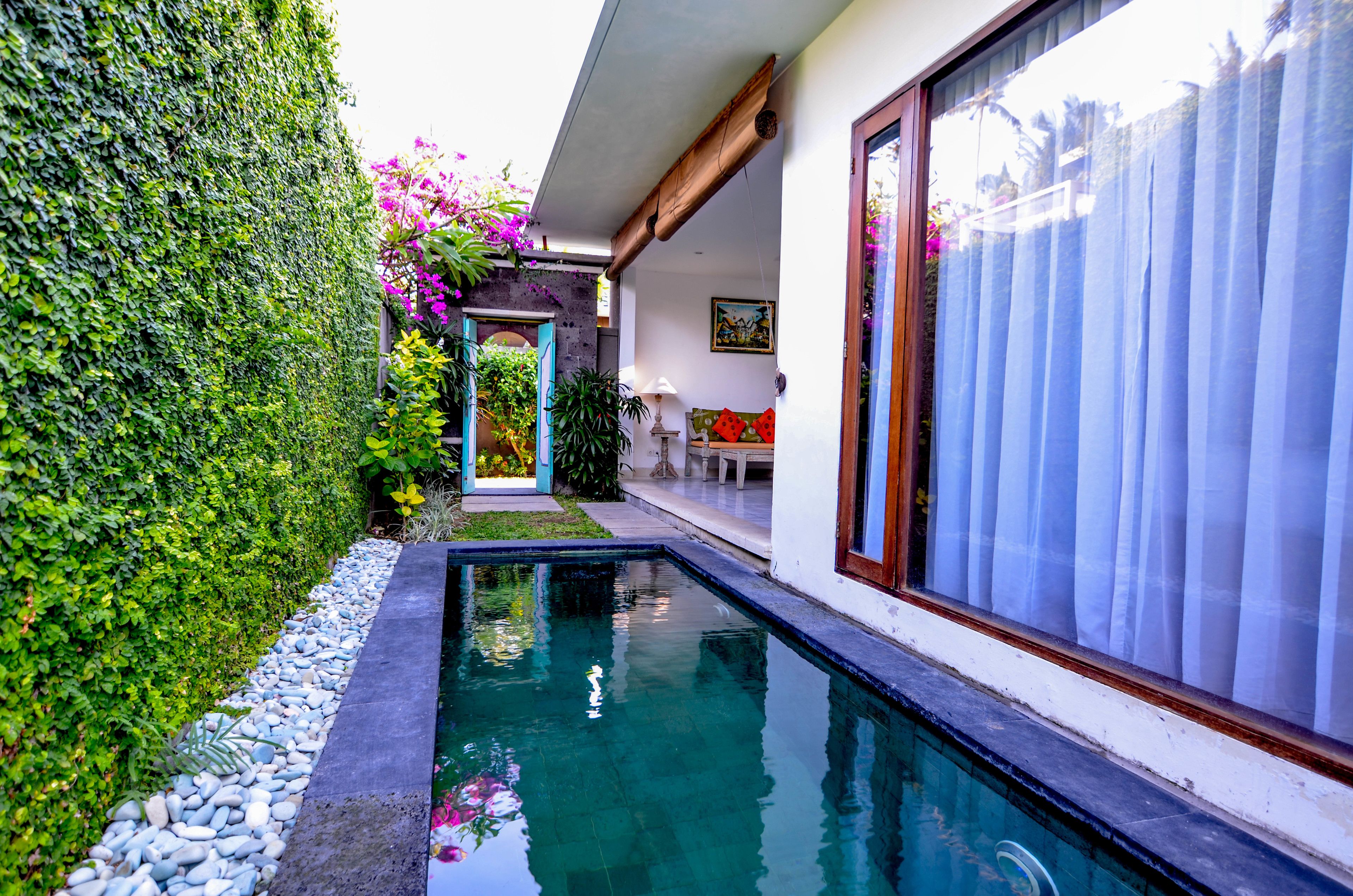 A swimming pool with a stone-lined edge, surrounded by a lush green hedge and a variety of plants.