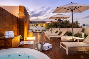 Una terraza en la azotea con jacuzzi, sillones y sombrillas.
