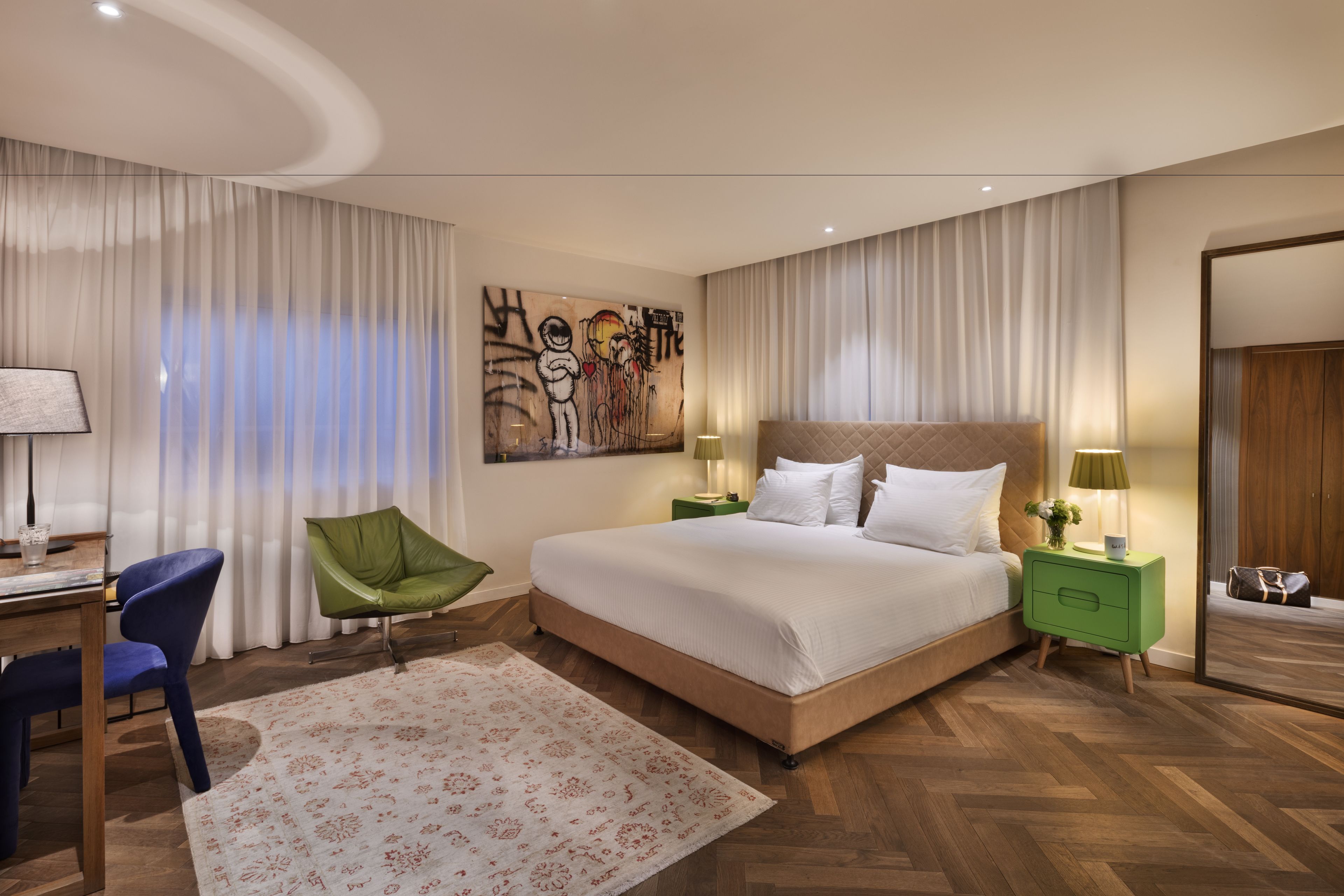 A modern bedroom with a large bed, green nightstands, a desk, and a chair.