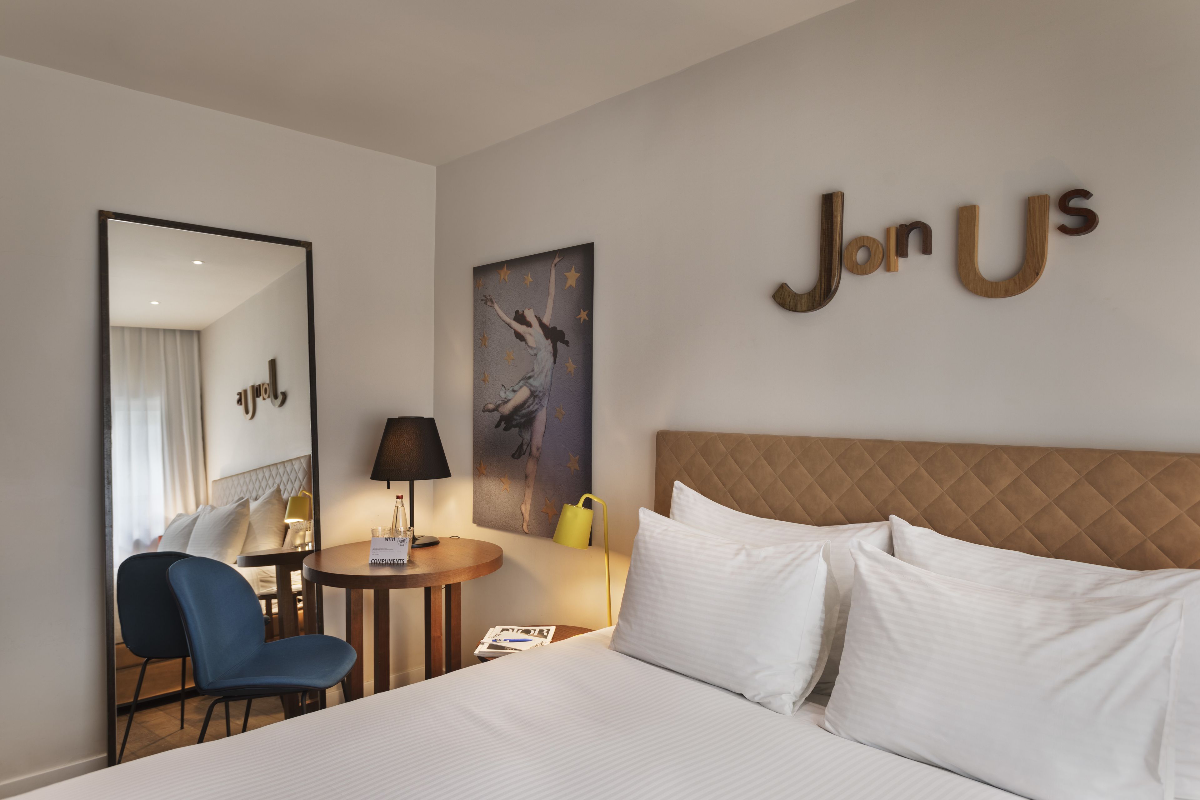 A hotel room with a bed, a desk, a chair, a lamp, and a painting.