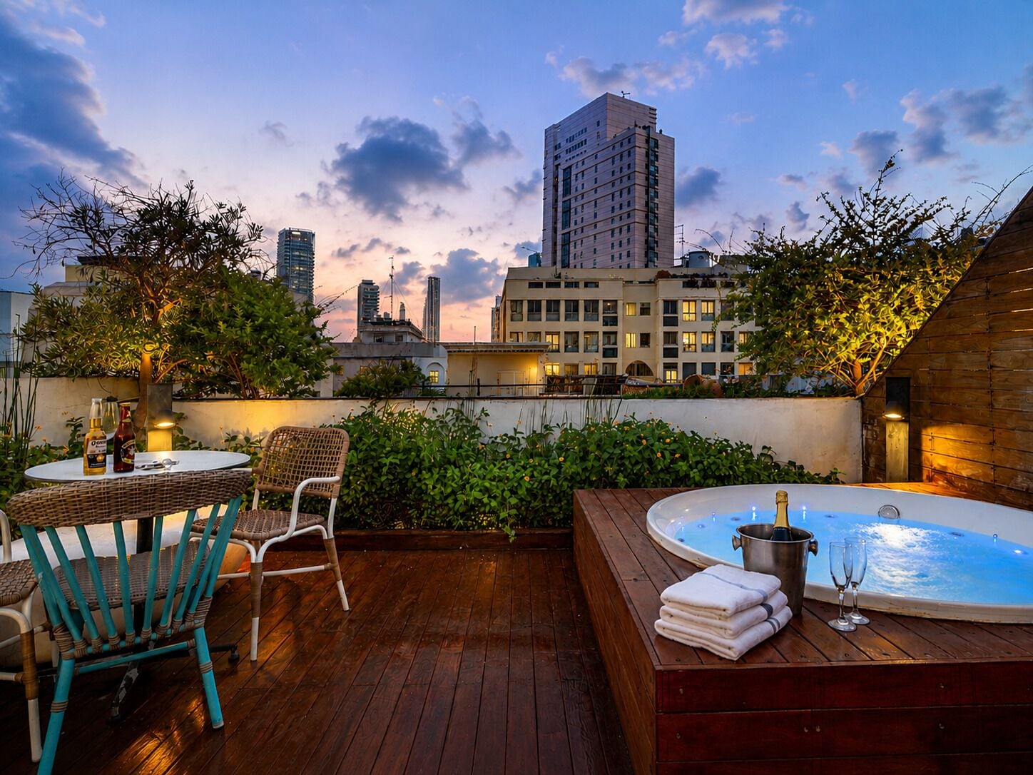 A rooftop terrace with a hot tub, lounge chairs, and a table with drinks.