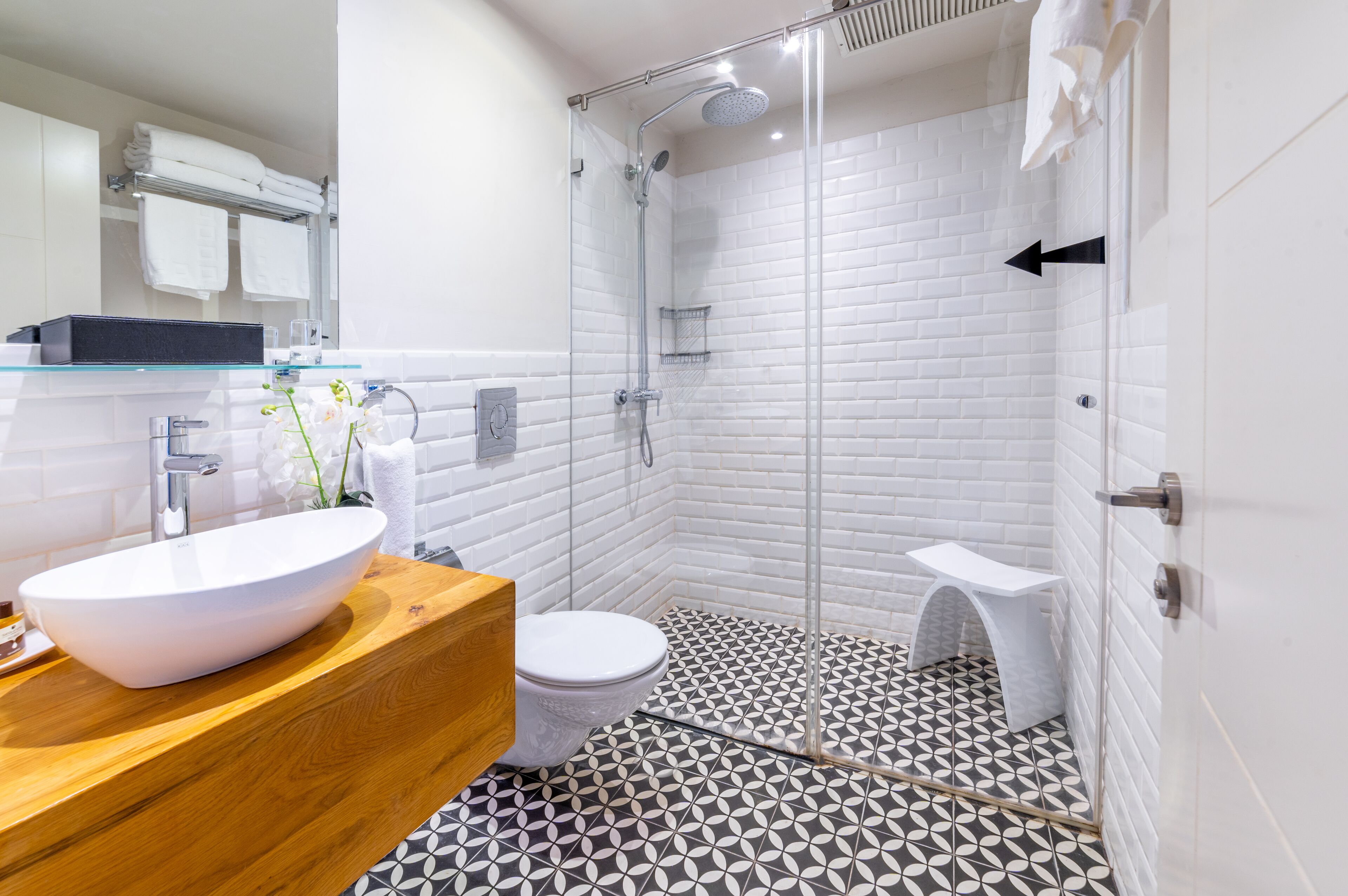 Un bagno moderno con cabina doccia in vetro, lavabo bianco e pavimento decorato.