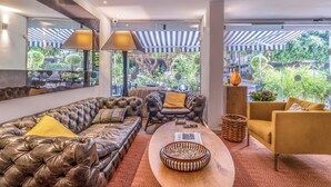 A modern living room with leather sofas, a wooden coffee table, and a view of greenery outside. - Jacob Shenkin Hotel (Tel Aviv)