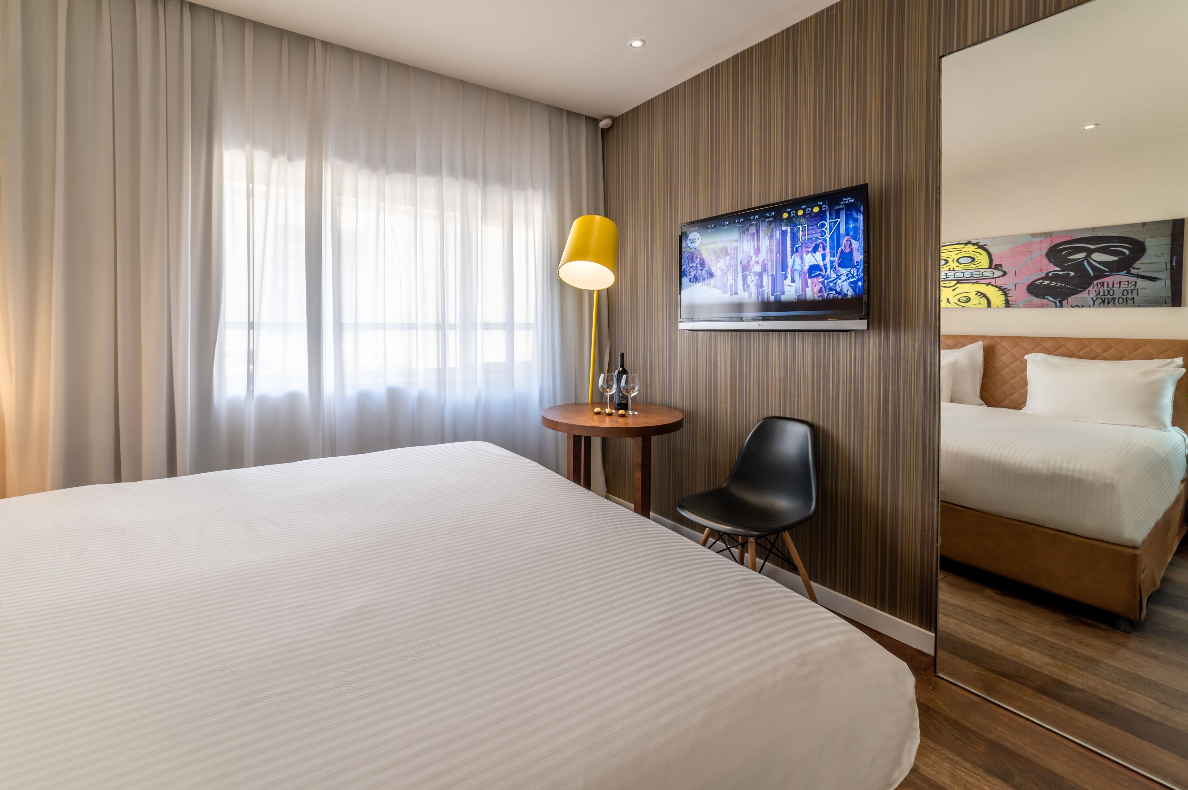 Habitación de hotel con una cama grande, un televisor montado en la pared, una mesita redonda con una lámpara y una silla.