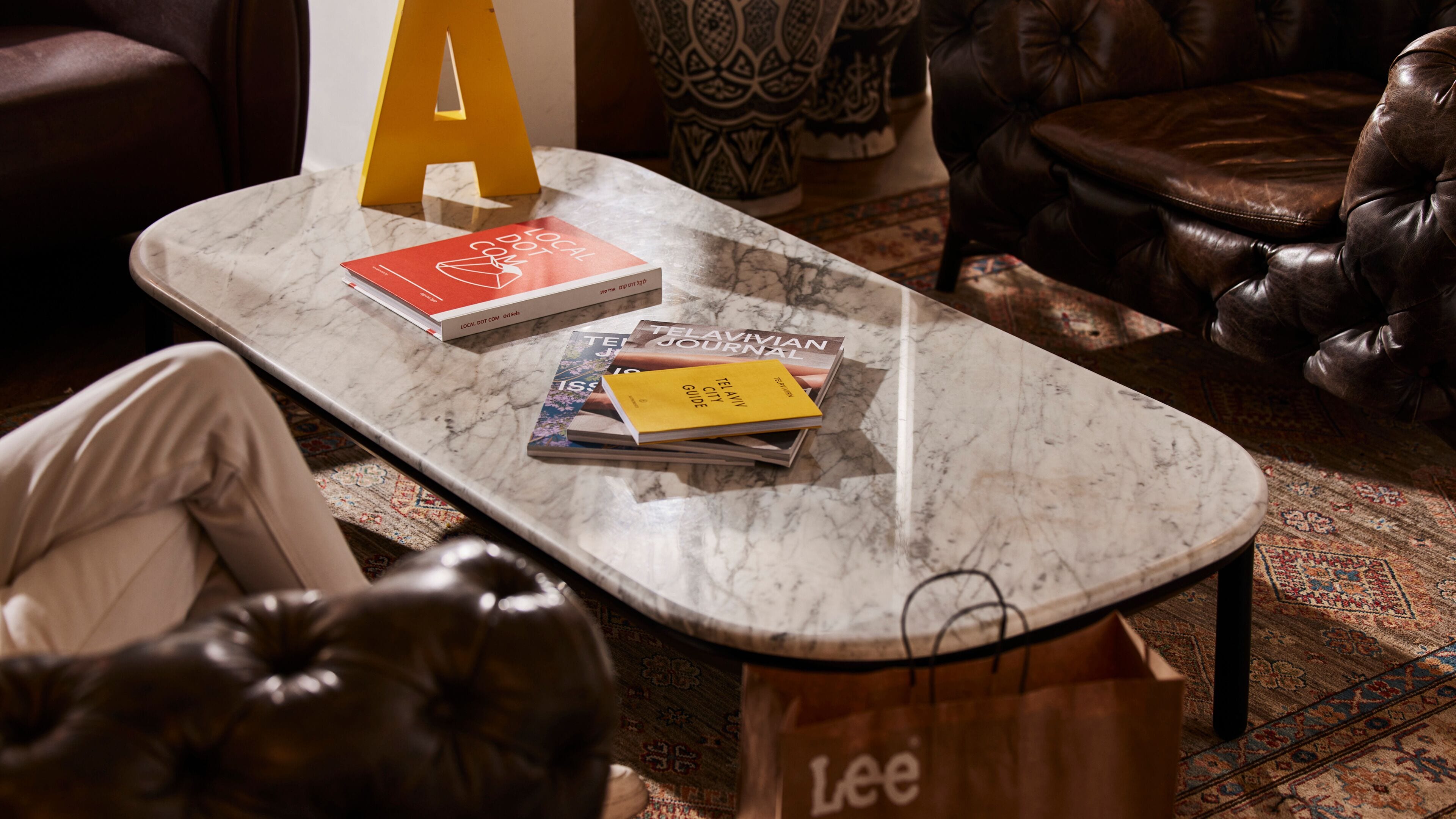 Una mesa de mármol con revistas y un libro amarillo, sillones de cuero y una alfombra estampada.