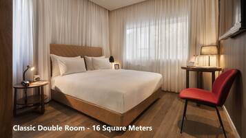 A classic double room with a large bed, bedside tables, a red chair, and a small table with a lamp.