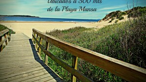 Um calçadão de madeira que leva a uma praia, com indicação de que o local fica a 300 metros da Playa Mansa.