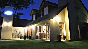 Uma casa moderna com entrada bem iluminada, grandes janelas e área externa espaçosa com vasos de plantas.
