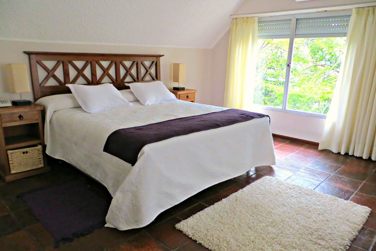A neatly made bed with a headboard, a bedside table with a lamp, and a window with curtains.