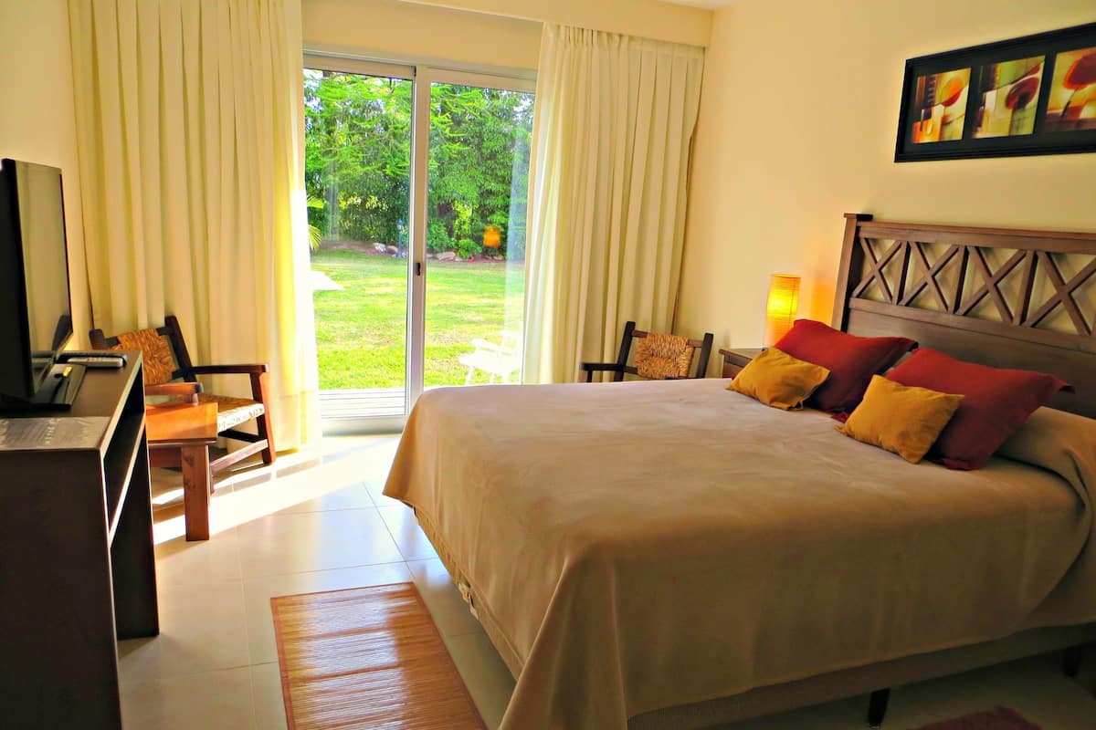 A hotel room with a bed, a desk with a computer, a chair, and a view of a garden through a sliding door.