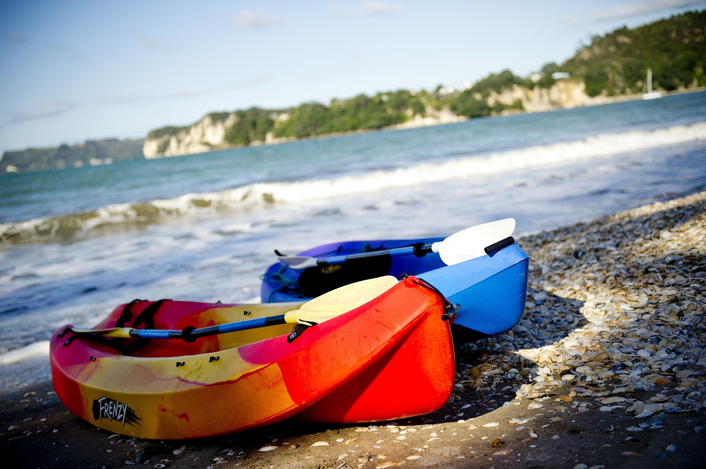 Dos kayak a una platja pedregosa amb vista al mar i penya-segats al fons.