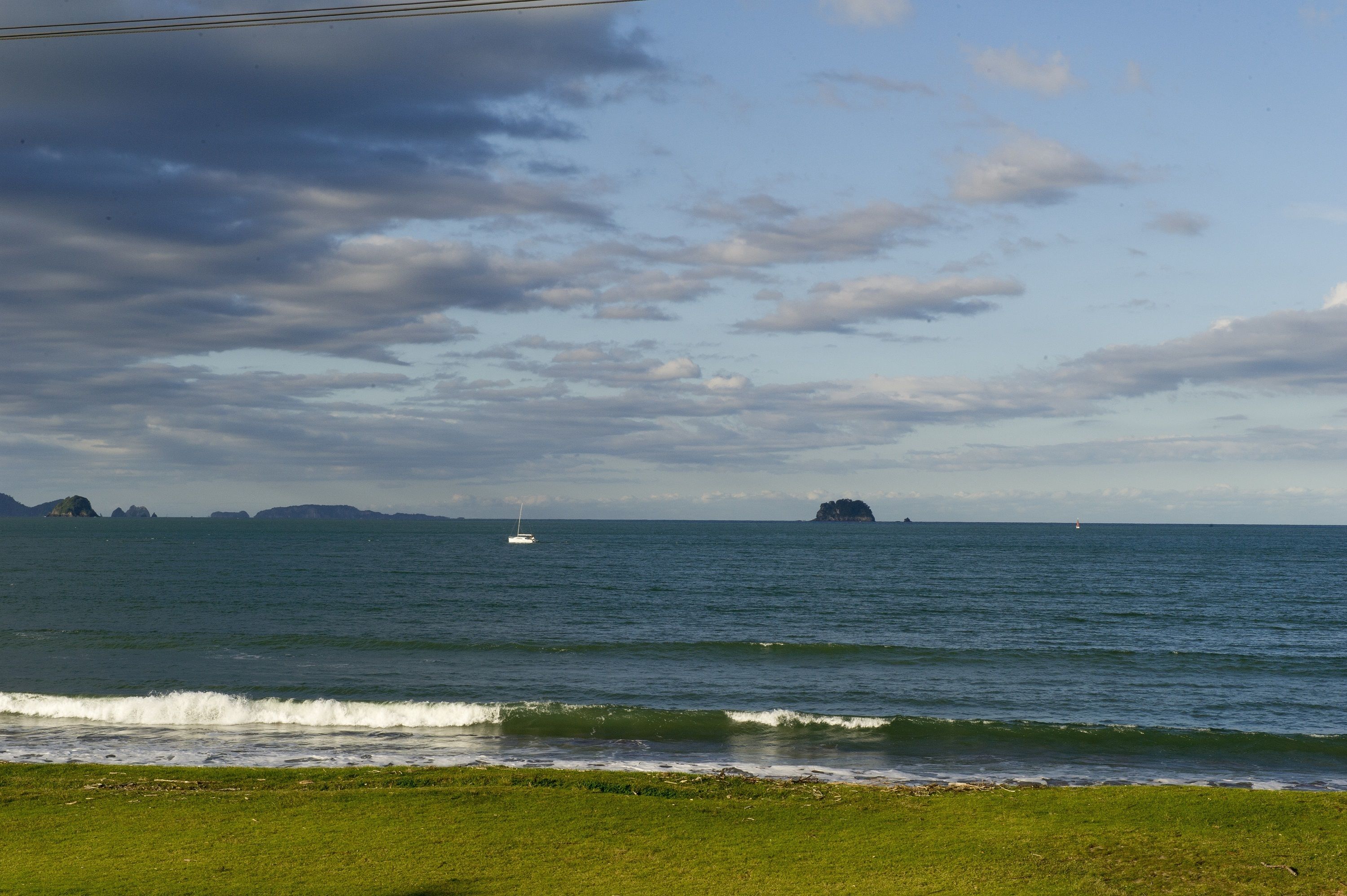 A coastal landscape with a grassy foreground, calm sea, and distant islands.