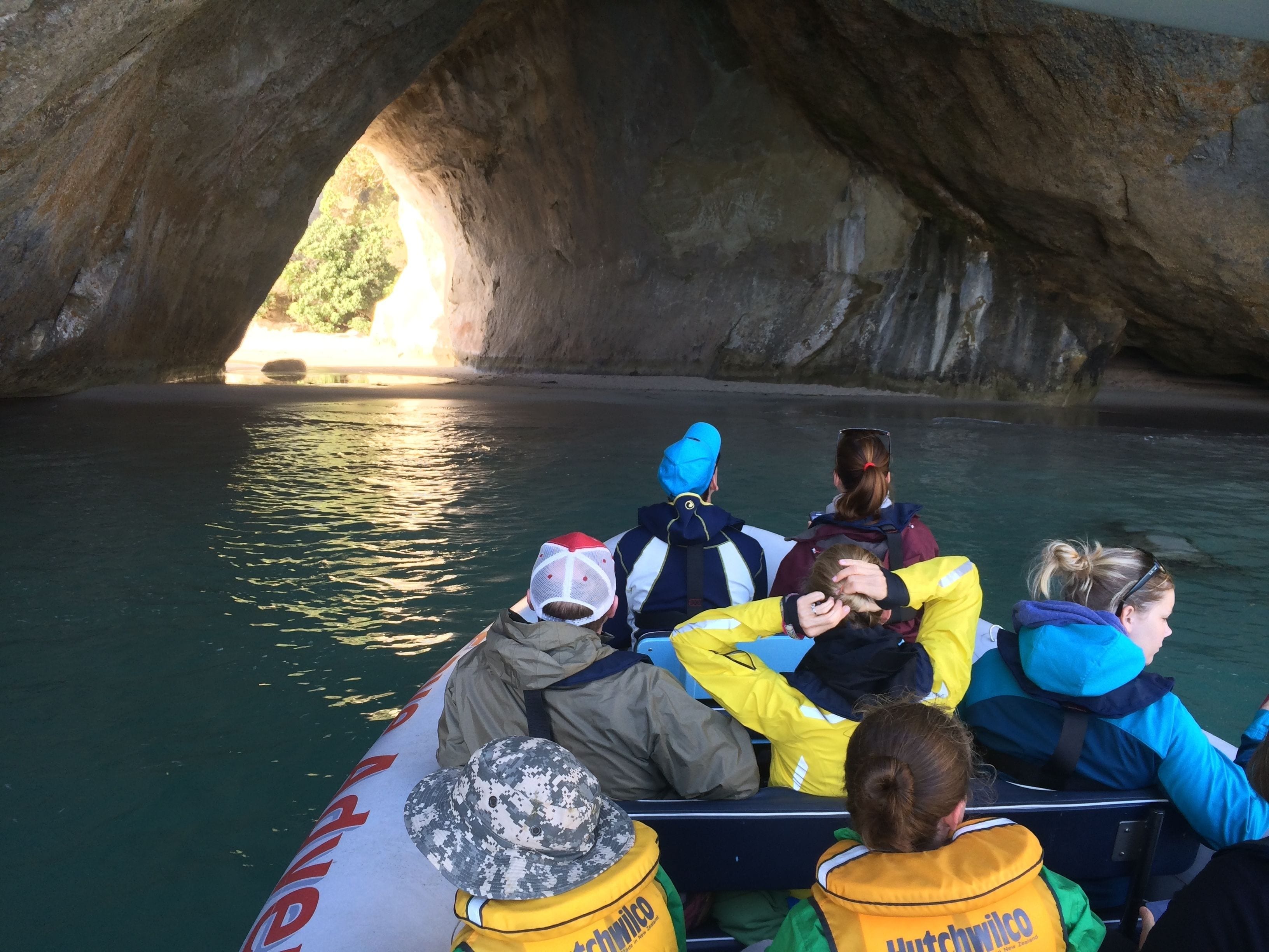 A group of people on a boat with a cave entrance in the background.