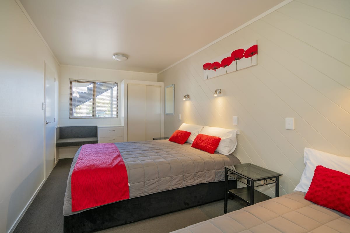 A modern bedroom with a large bed, a small bedside table, and a window with blinds.