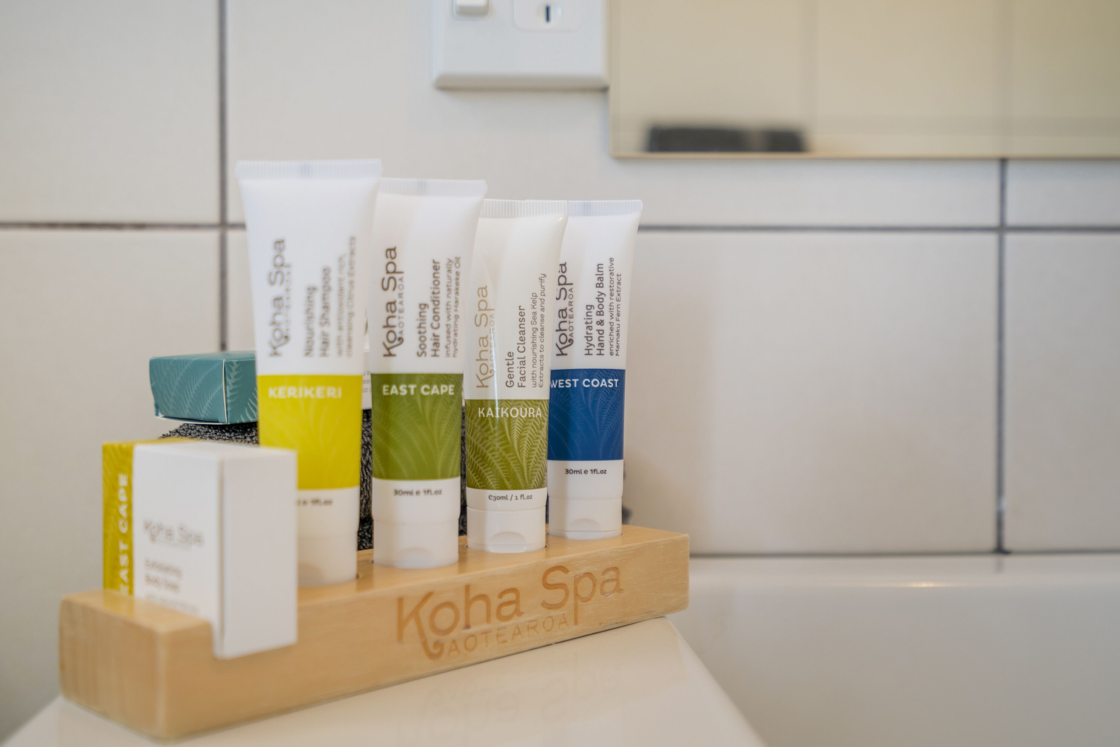 A wooden display stand with various Kōha Spa products in a bathroom setting.