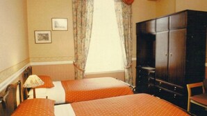Une chambre d’hôtel avec deux lits, une armoire, un bureau et une fenêtre avec des rideaux.
