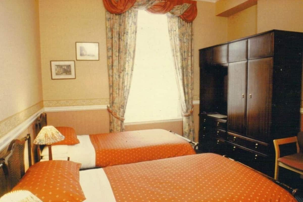 A hotel room with two beds, a wardrobe, a desk, and a window with curtains.