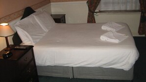 Un lit bien fait, avec du linge de lit blanc, une lampe de chevet et une petite table de nuit en bois.