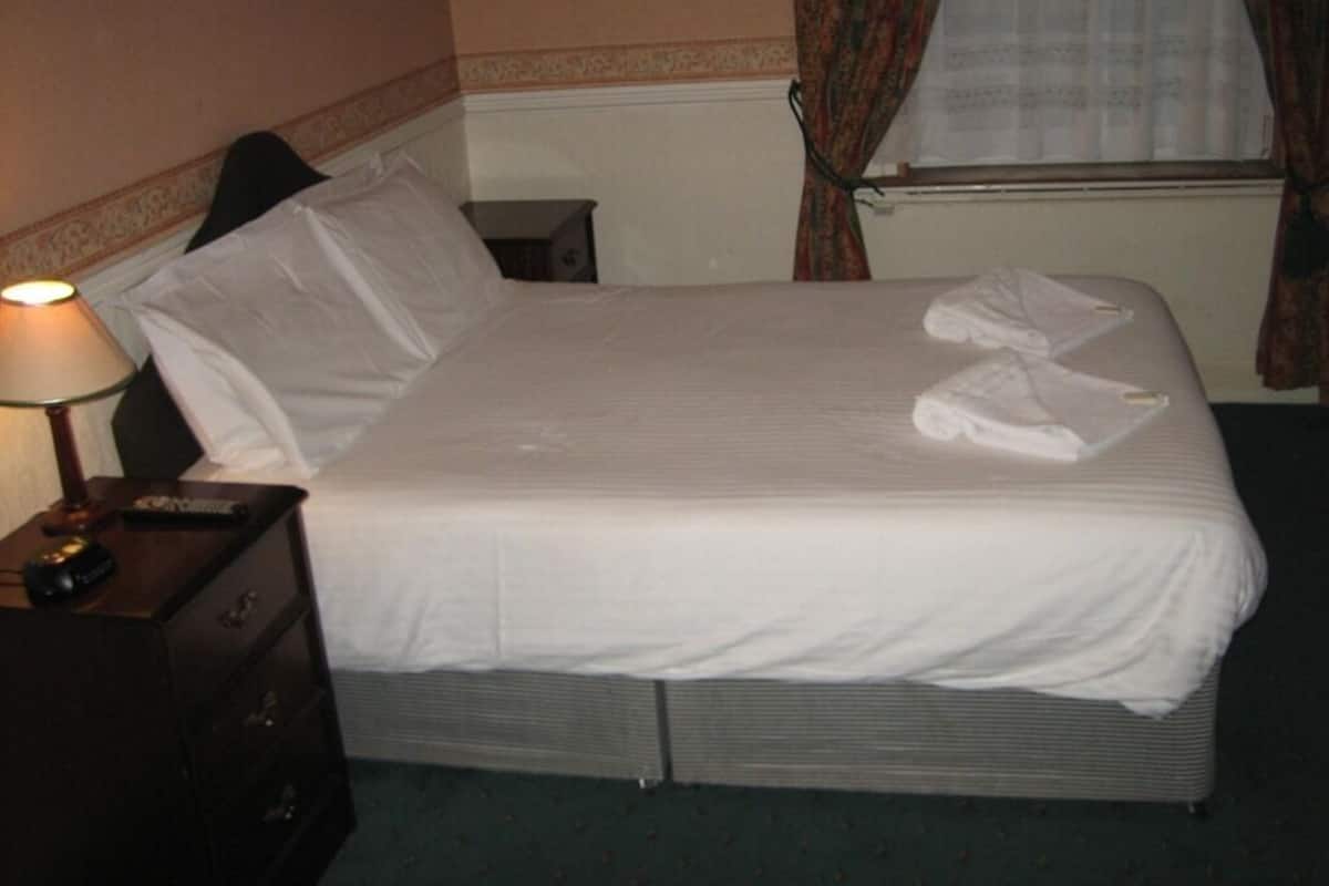 A neatly made bed with white linens, a bedside lamp, and a small wooden nightstand.