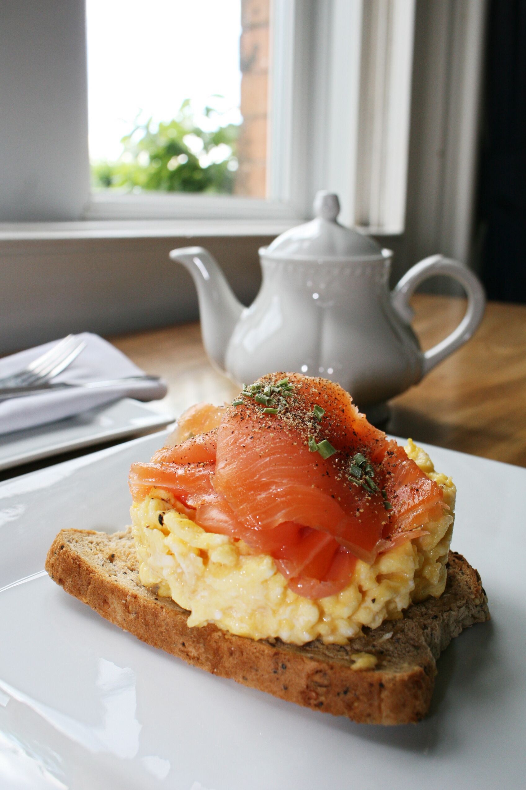 Un plato de desayuno con huevos revueltos, salmón ahumado y una ramita de hierbas sobre una rebanada de pan integral.