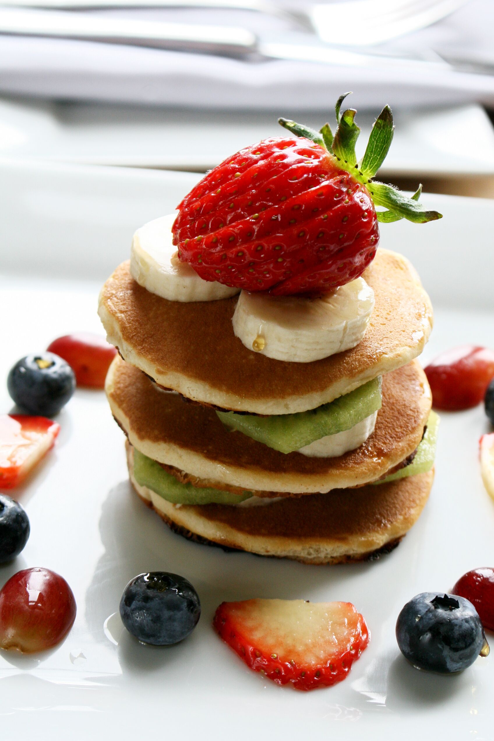A stack of pancakes with strawberries and bananas on top, surrounded by berries.