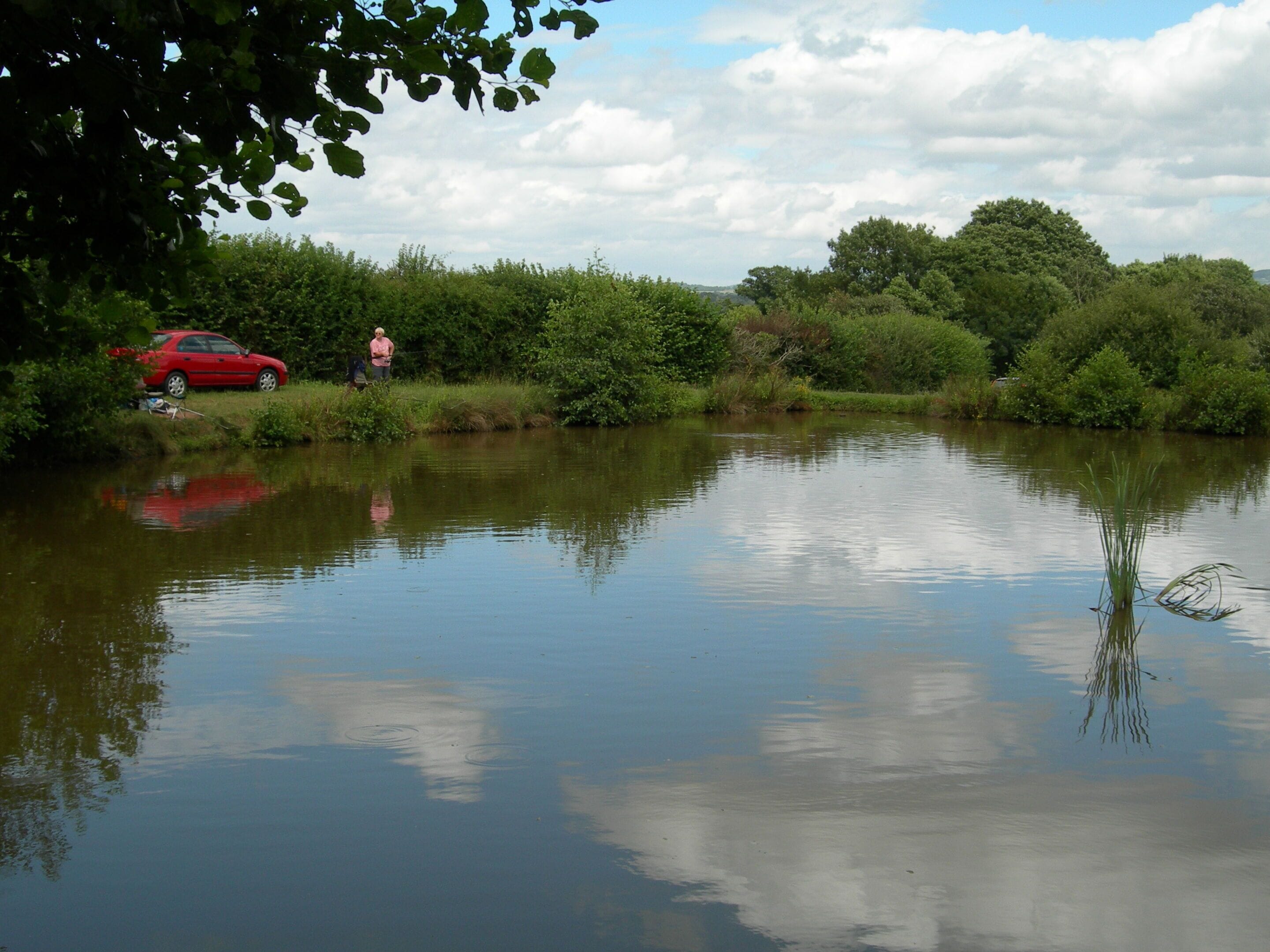 A calm river with a red car parked on the bank and a person standing nearby.