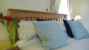 Una cama bien hecha con cabecera de madera, un jarrón con tulipanes rojos sobre una mesita de noche y una lámpara en la mesilla.