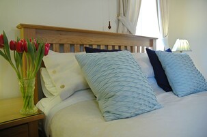 Una cama bien hecha con cabecera de madera, un jarrón con tulipanes rojos sobre una mesita de noche y una lámpara en la mesilla.