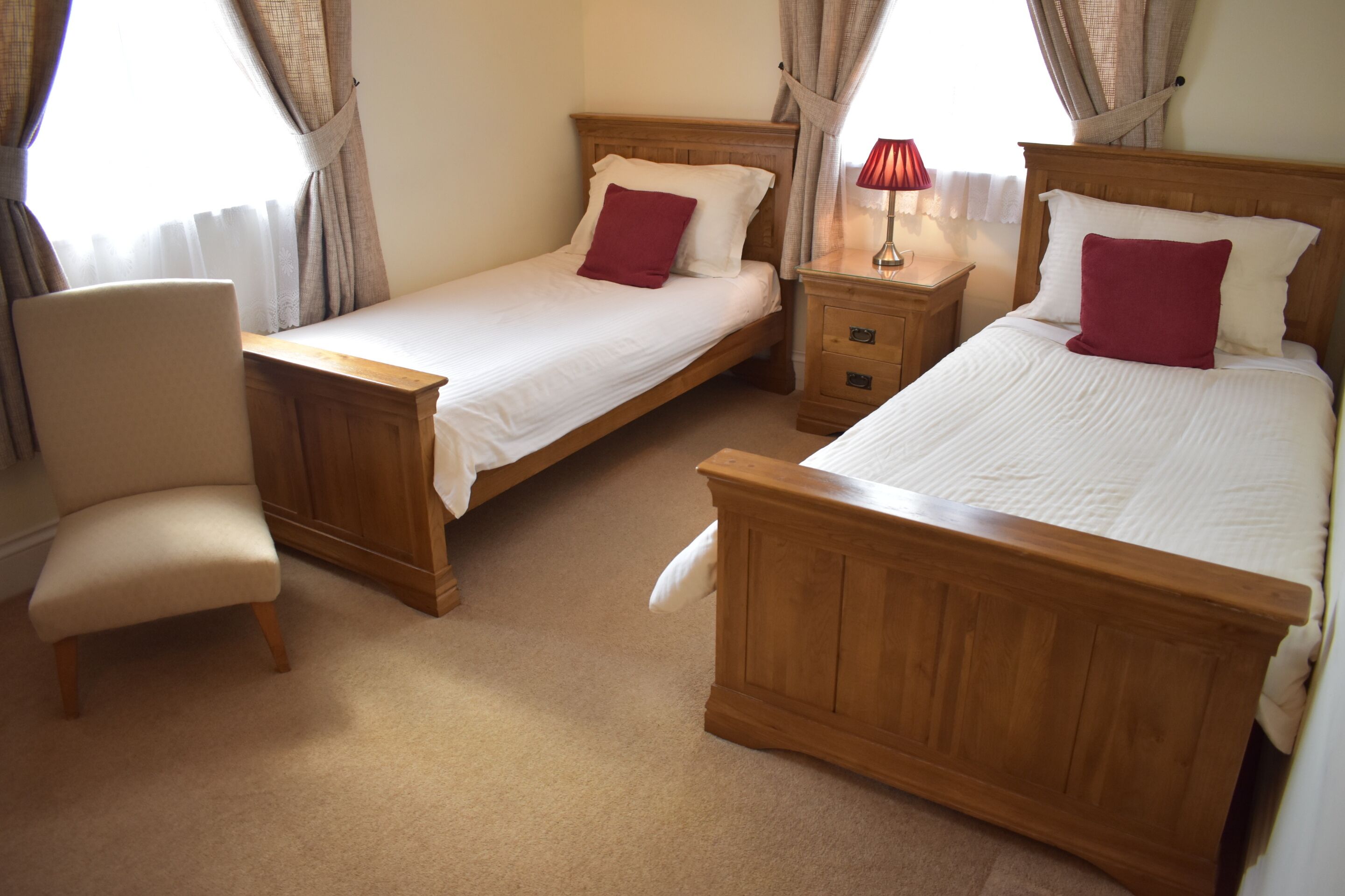 A hotel room with two single beds, a wooden nightstand, a chair, and a window with curtains.
