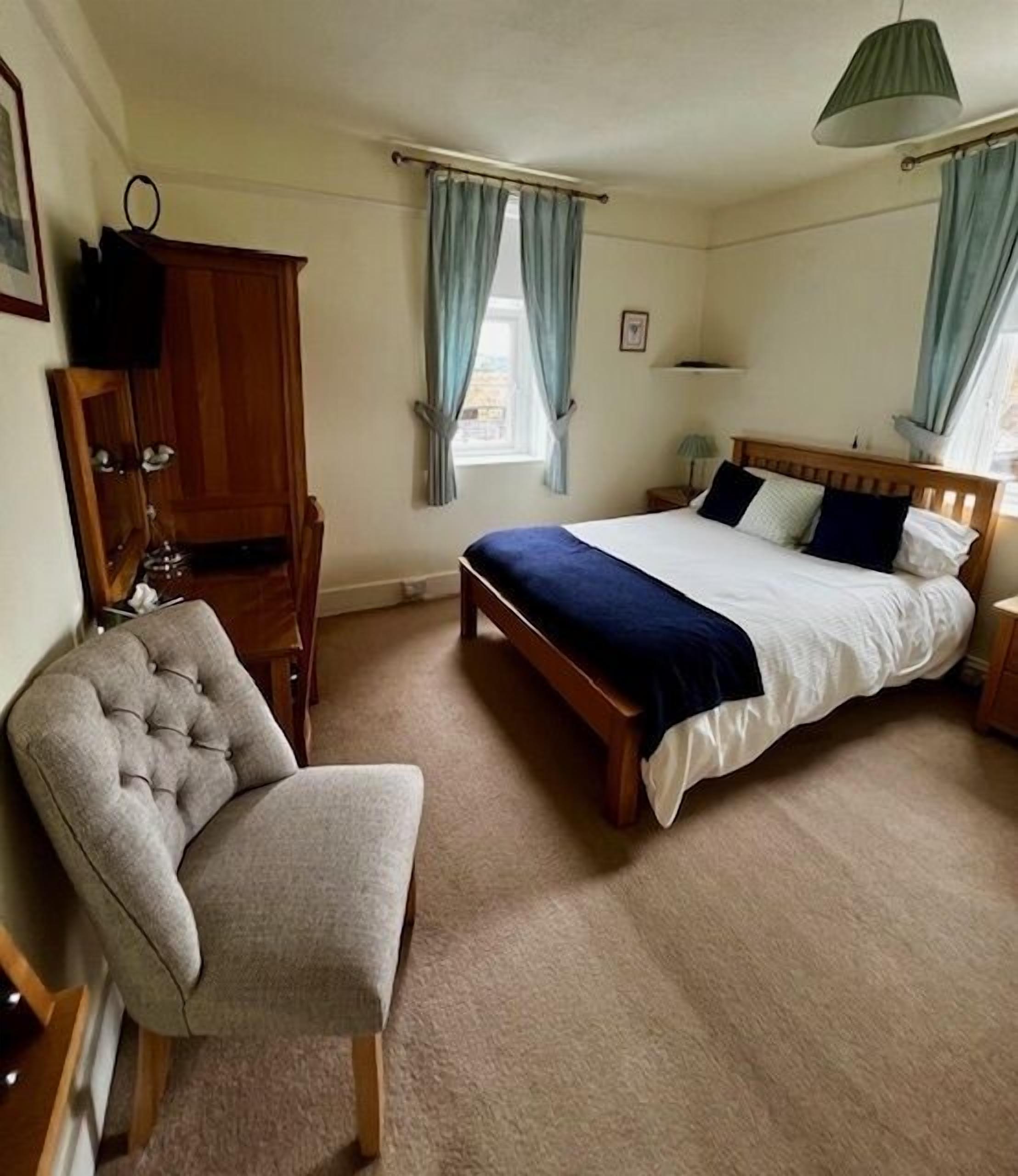 A bedroom with a bed, a chair, a wardrobe, and a window with curtains.